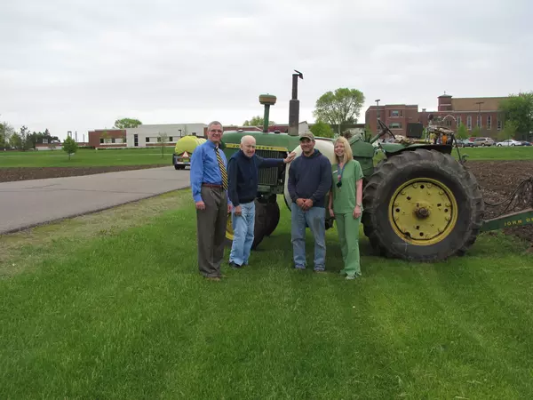 Four people standing in front of John Deere tractor at Gundersen St. Elizabeths field of dreams.