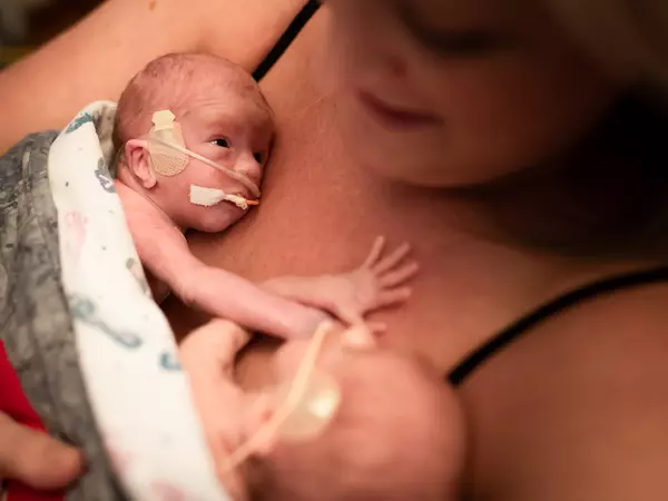 Premature twins held skin to skin by mother in hospital NICU.