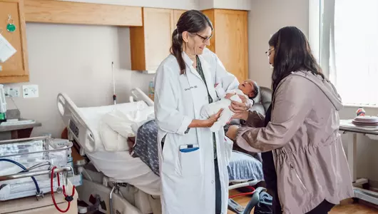 Doctor handing newborn to mother.