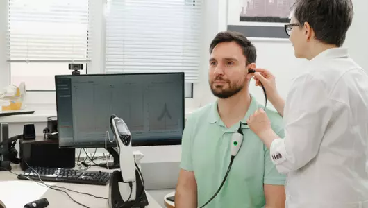 Audiologist testing patient for hearing loss in exam room.