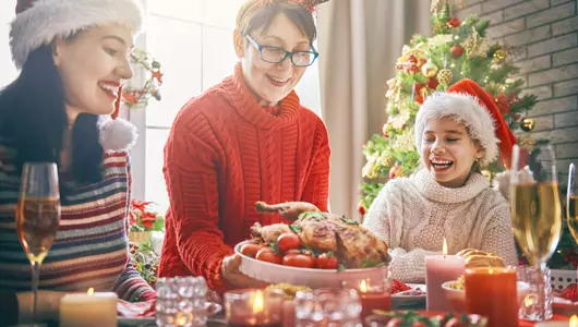 eating well during the holidays - family sitting at a table about to eat a holiday dinner.'