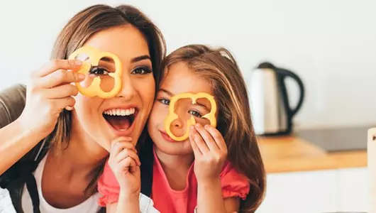 smiling mom and daughter holding a slice of pepper over an eye