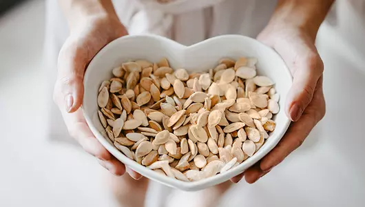 Woman holding a heart shaped bowl of roasted pumpkin seeds