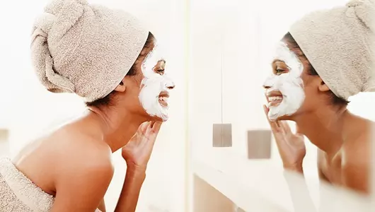 smiling woman applying face mask while looking in mirror