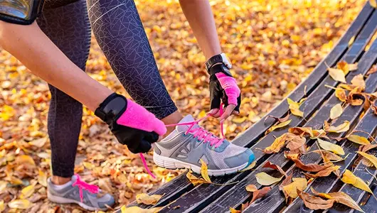 woman tying workout shoes in yellow fall leaves